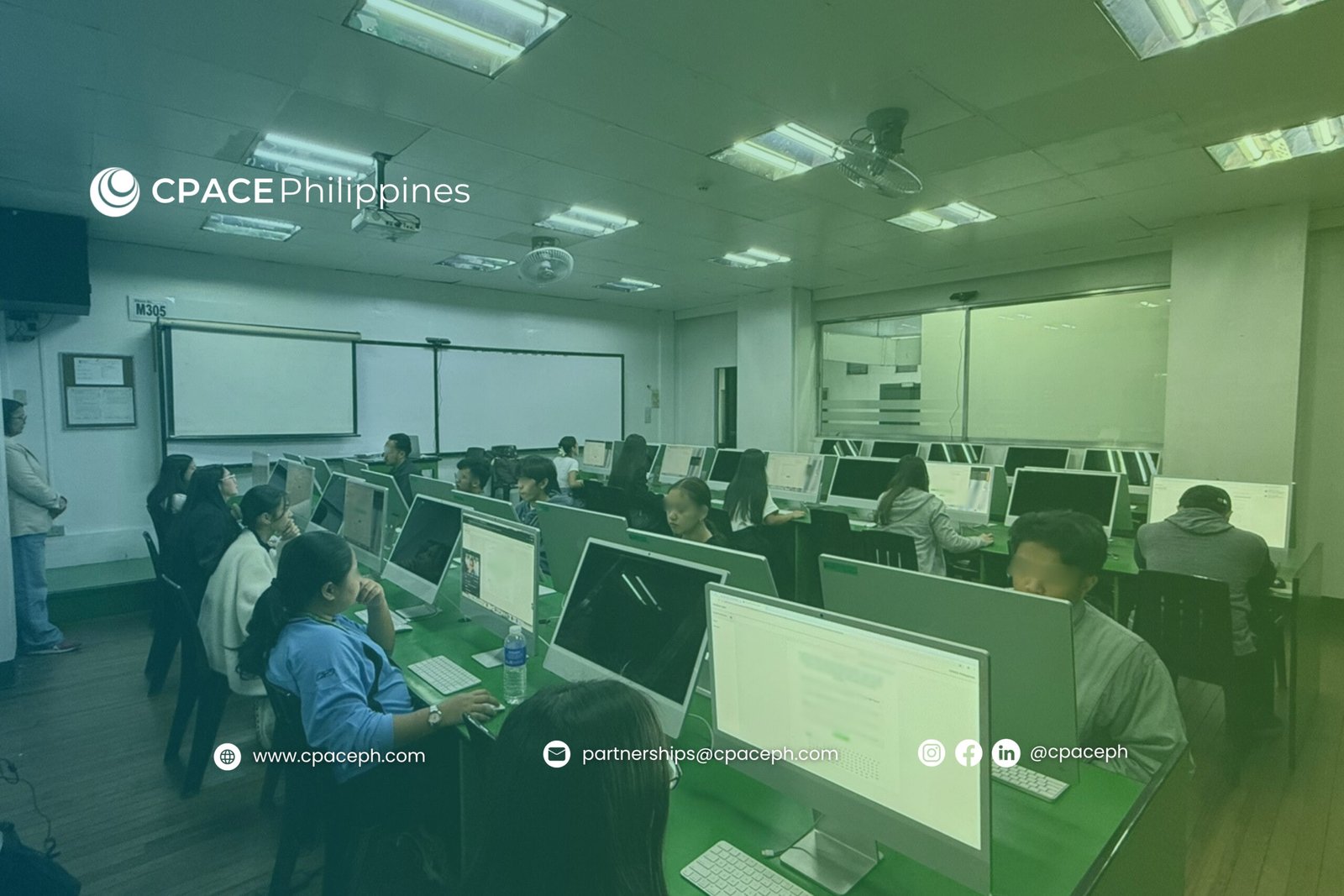 Computer laboratory with rows of desktop computers, participants engaged in training session, instructor standing near whiteboard and projector screen, CPACE Philippines branding visible on wall.