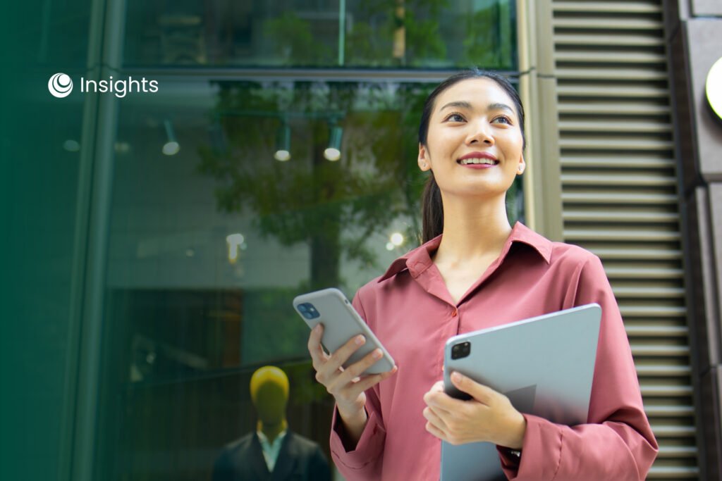 A smiling woman in professional attire walking outdoors while holding a smartphone and a digital tablet, with "Insights" logo in the top left corner.