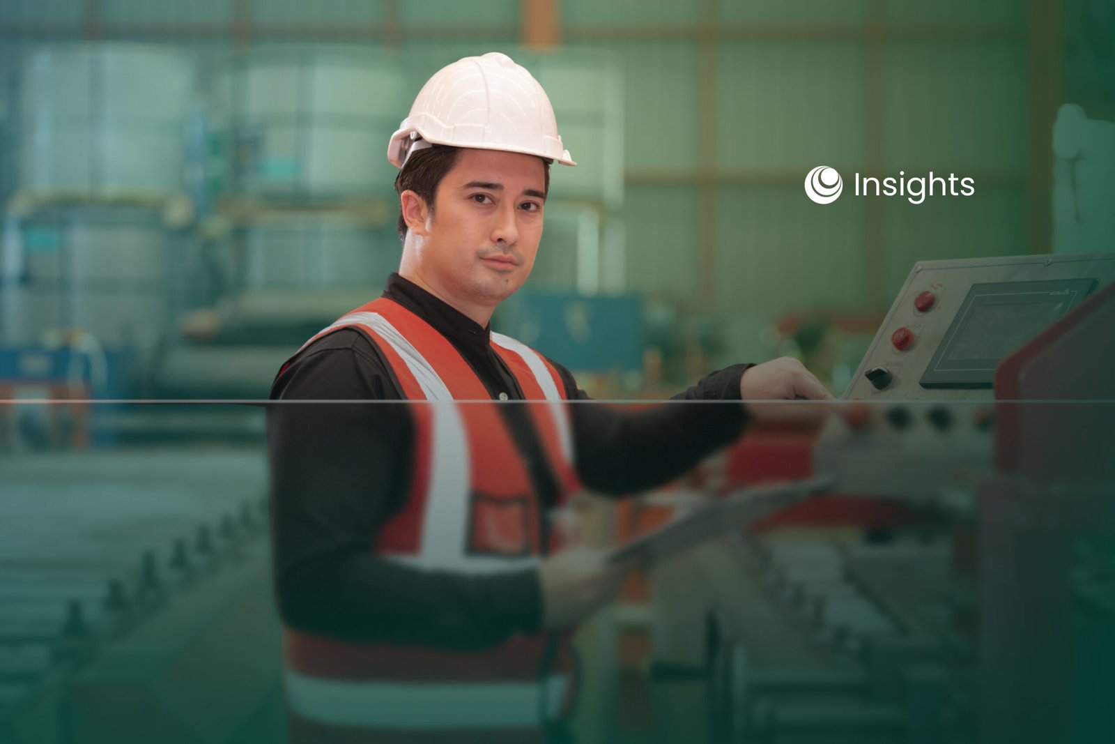 A male factory worker wearing a hard hat and reflective vest operating industrial machinery.