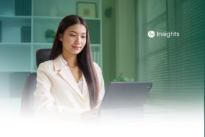 A professional woman in a white blazer working on a tablet at her office desk.